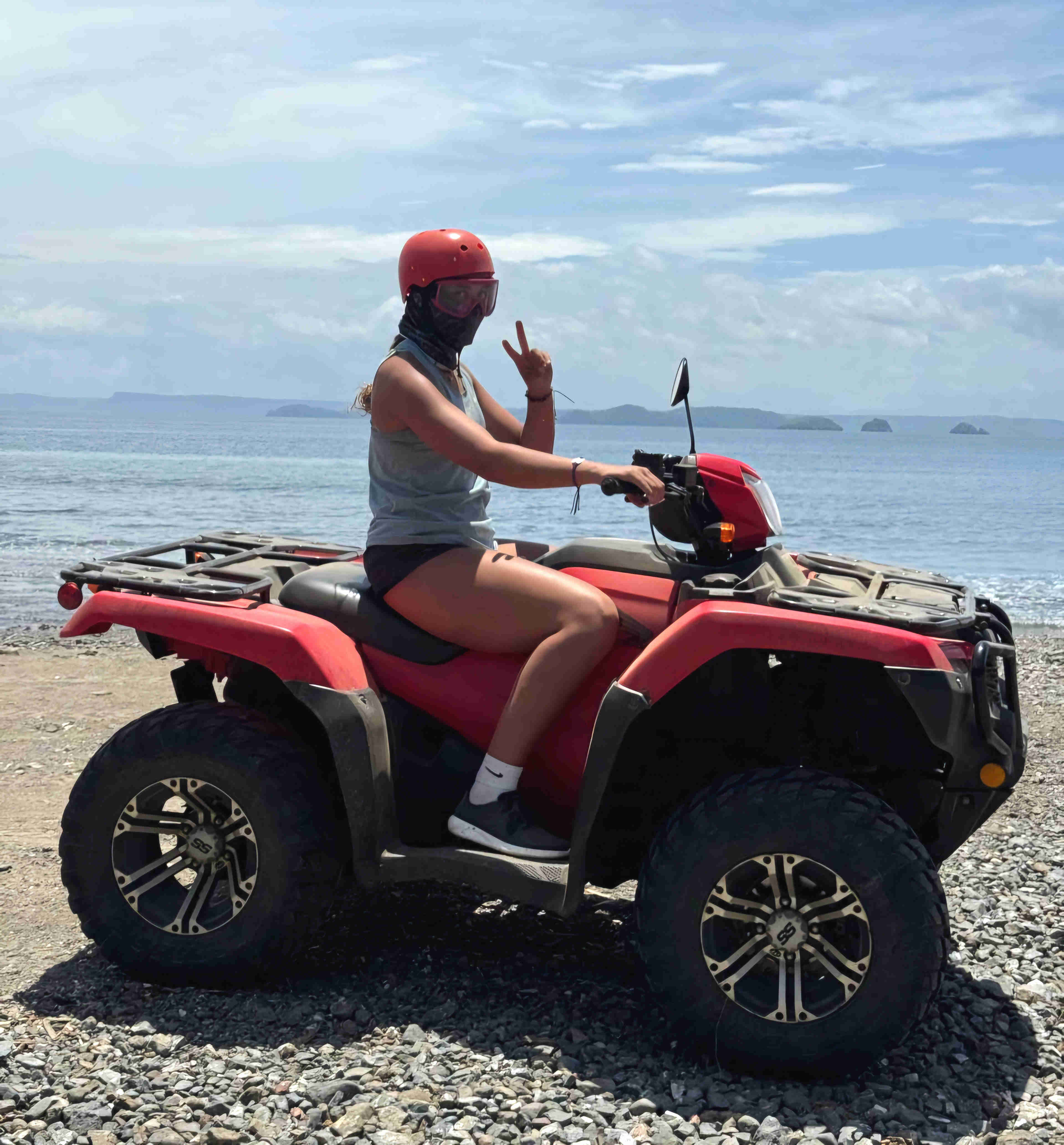 Person riding a red ATV on a beach in Guanacaste, Costa Rica, with ocean and islands in the background, part of the ATV and monkey sanctuary tour  