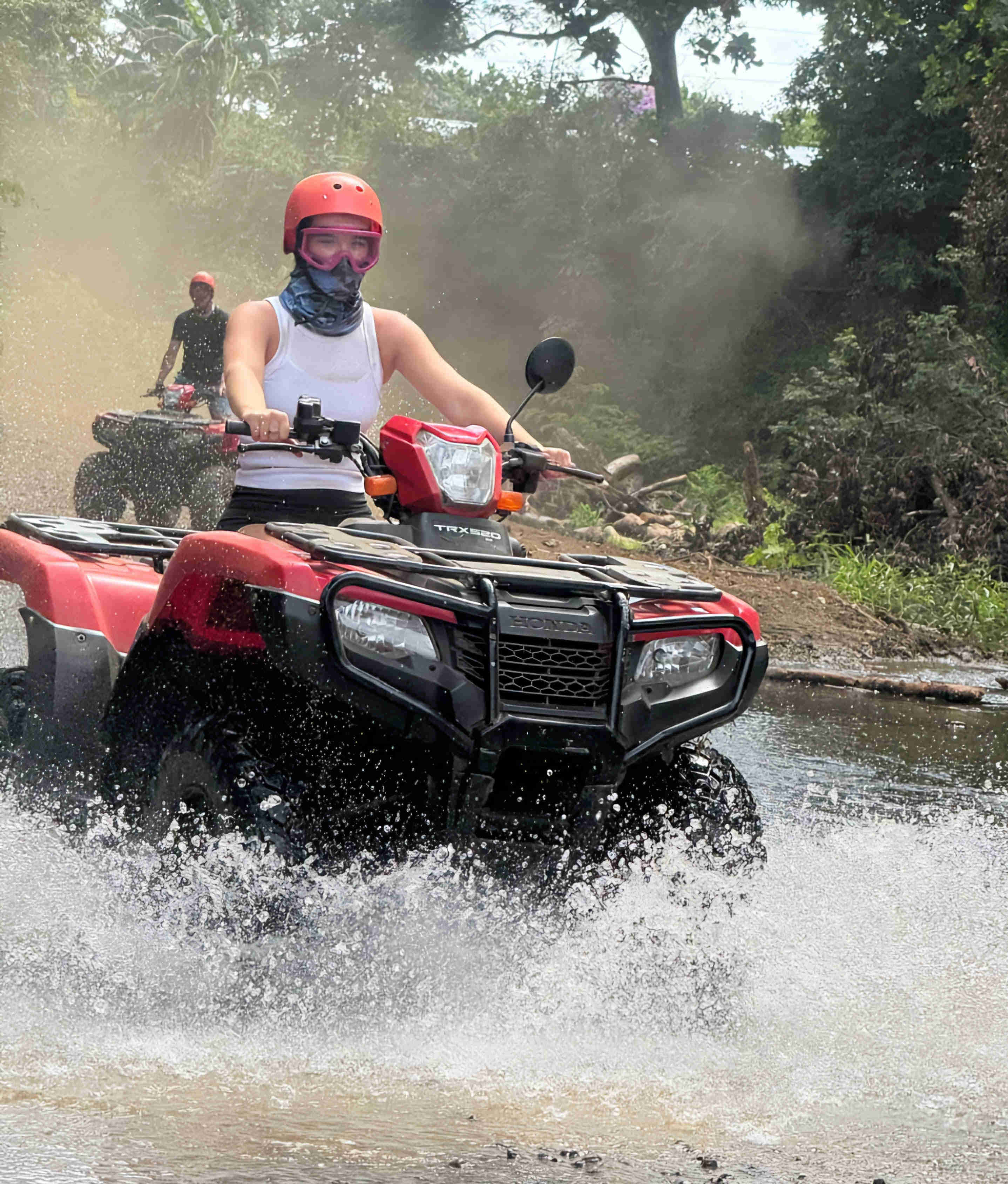 Woman riding atv through jungle river crossings, splashing water on high in the air