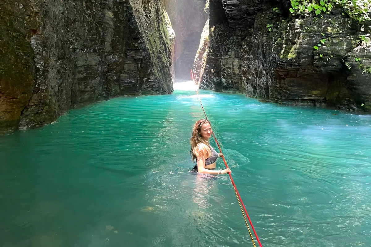 Woman swimming through the narrow turquoise canyon with a guide rope toward La Leona Waterfall on a guided adventure tour in Guanacaste, Costa Rica