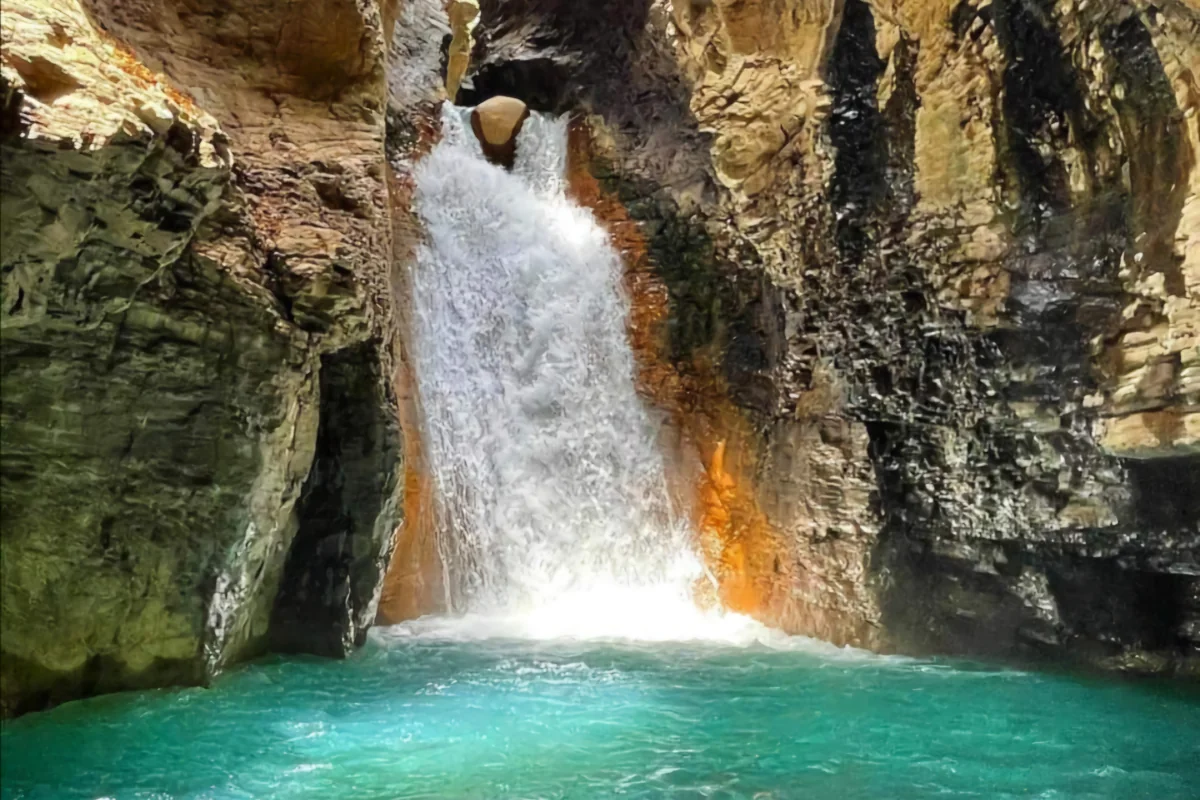 Crystal clear turquoise pool at the base of La Leona Waterfall surrounded by volcanic rock canyon walls in Guanacaste, Costa Rica